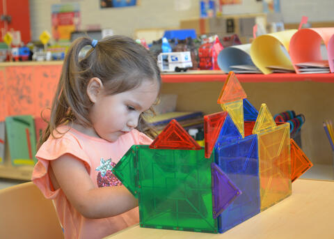 A child plays builds a colorful structure on a table.