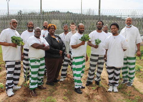 Men in prison garb hold vegetables outside.