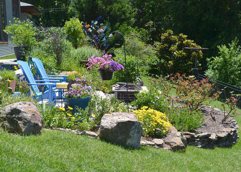 Two blue chairs in a garden are surrounded by flowers.
