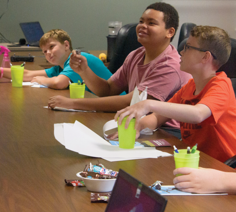Three smiling elementary students sit at a conference table.