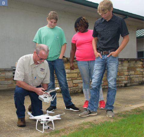An adult shows three teenagers how to fly a drone.