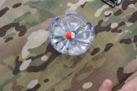 The bottom half of a clear drink bottle holds water and a small piece of fishing cork with a sewing needle pushed through it.