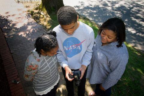 Overhead shot of a young boy holding a camera standing between two women.