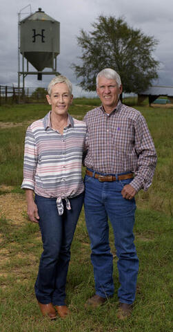 A couple standing in a grassy field with arms around each other.