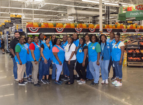 A large group of Walmart employees wearing blue vests smiling for a group photo.