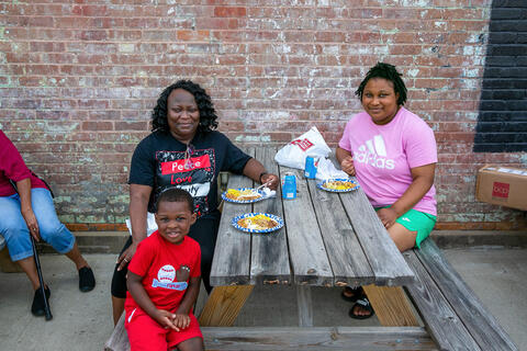A woman, with a girl and a boy, sitting at a picnic table with food in front of them.