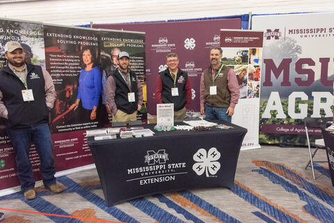 Four men stand at Mississippi State University Extension Service booth.