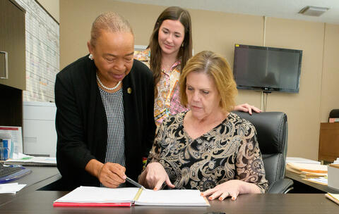 A person points at a ledger while two other people look on.