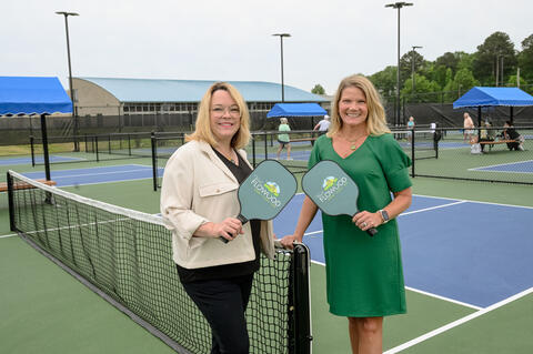 Two smiling people holding paddles stand on a pickleball court.
