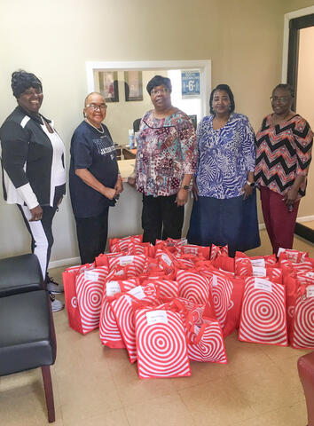 Five people stand behind a large group of red bags with white circles.
