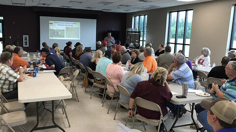 Extension agent explains weed management to a crowded room of people learning about best management practices for goats