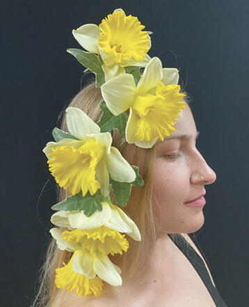 Side profile of woman wearing a headpiece of five large yellow flowers and leaves.