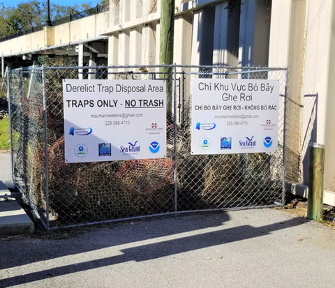 A fenced derelict trap disposal area filled with metal traps. Signs in English and Vietnamese instruct people to place only traps inside the fence, not trash.