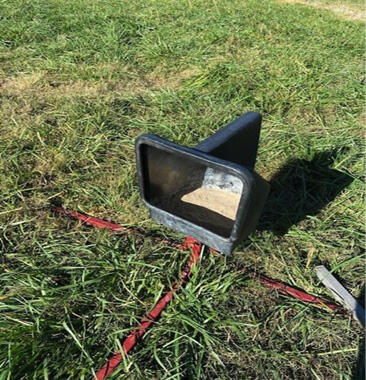 A black, plastic feeder in a grassy area.