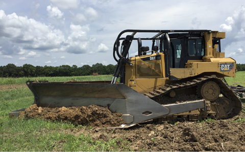 A bulldozer with a large attachment removes stems in a field.