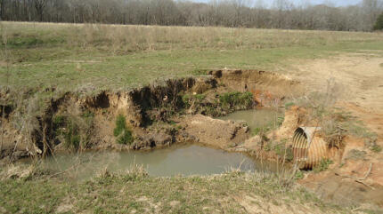 Figure 3A before: Eroded ground with an exposed drainage pipe and pools of water.