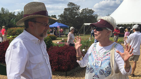 Extension specialist talks with a woman in a raised bed flower garden during an outdoor gardening seminar