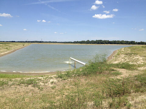 A low-lying storage pond with a white pipe pouring water into the pond. 
