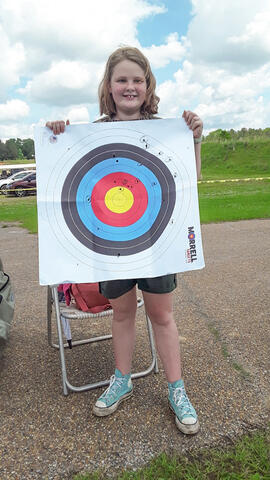 A standing child holding an archery target, showing where the arrows struck.