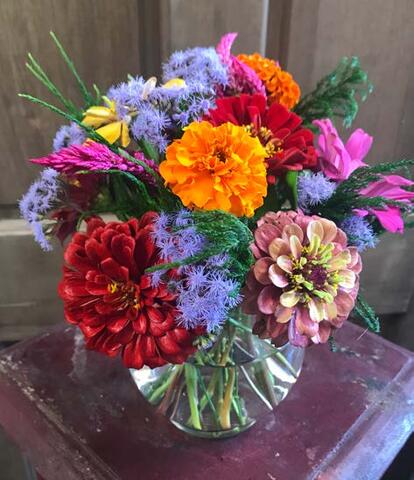 A completed Sweet Mississippi floral design. It includes different brightly colored flowers and greenery in a glass bowl-type vase.