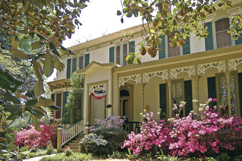 Victorian house with bright-pink azaleas and other landscaping along the front porch.