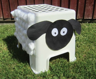 A white stepping stool with a face and ears made from black construction paper and cotton balls in five rows on the side of the stool.