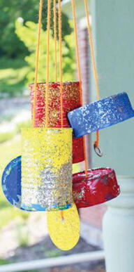 Jar tops and cans are painted and hanging by strings outside.