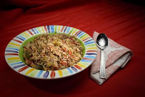A bowl of Italian ground beef and rice in a rainbow-striped bowl sits on a red tablecloth with a red and white cloth napkin and a spoon.