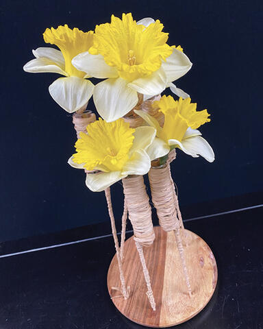 Four yellow and white flowers affixed upright to a circular wooden base. Refer to Table Arrangement section for more details.