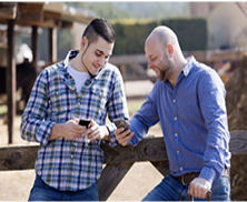 Two men are looking at their phones while standing outside.