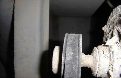 Closeup of a black fan belt positioned around a worn pulley.