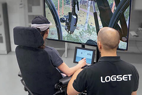 A student sits in a simulator while a trainer provides instructions.