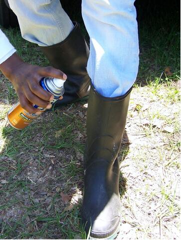 A person sprays repellent on boots with jeans tucked into them.