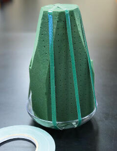 Cone-shaped foam brick with vertical bands of tape that attach the brick to the glass dish.