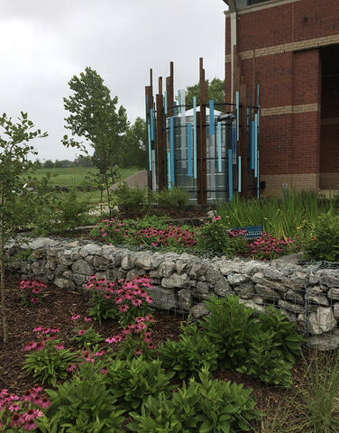 A garden of flowers and shrubs with stacked rocks and fencing in the middle is next to a facility.