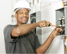 A man wearing a hard hat works on an electrical box.