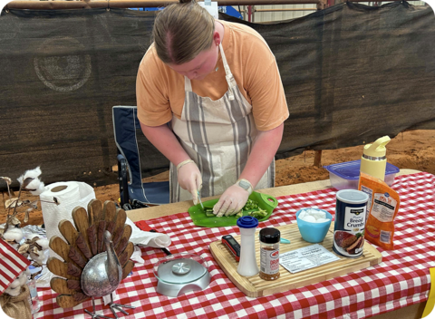 A contestant cuts peppers on a decorated table with many other ingredients.