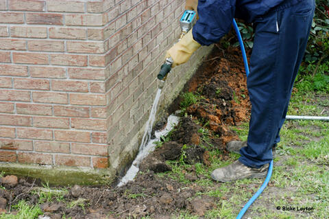 A pest control technician applies a termiticide around the exterior foundation of a home.