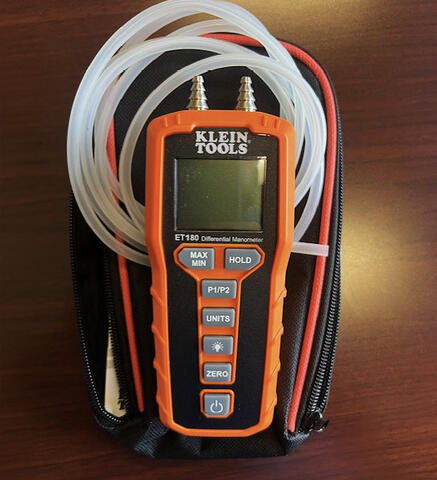 A digital differential manometer resting on silicon tubing and storage pouch.