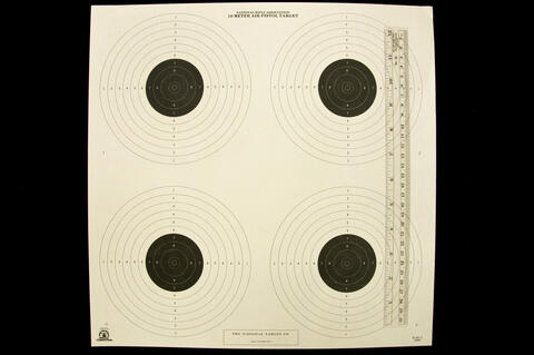 National Rifle Association 10 Meter Air Pistol Target with four targets with six white outer circles and five smaller inner black circles with a ruler lying vertically on the right of the target.