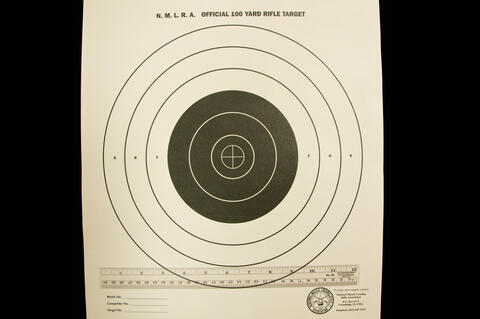 N. M. L. R. A. Official 100 Yard Rifle Target with seven circles getting wider as they go outward with three of them being white on the outside and the other four being black towards the middle.