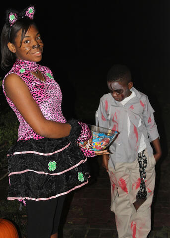 Two children dressed in costume with a bowl of candy while trick or treating.
