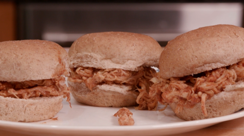 Three small sandwiches made with whole wheat slider buns, shredded chicken, and barbecue sauce on a white plate.