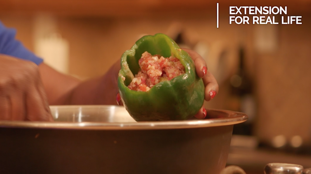 Hands spoon a ground meat and riced cauliflower mixture into a raw green bell pepper held over a stainless steel bowl. Hands spoon a ground meat and riced cauliflower mixture into a raw green bell pepper held over a stainless steel bowl.