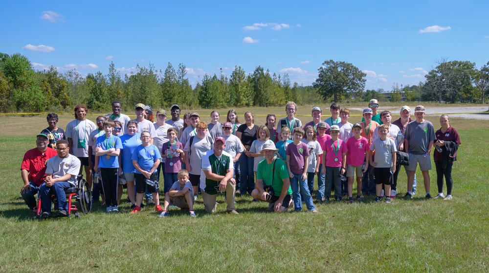Adults and young people standing in a group on a grassy plain.