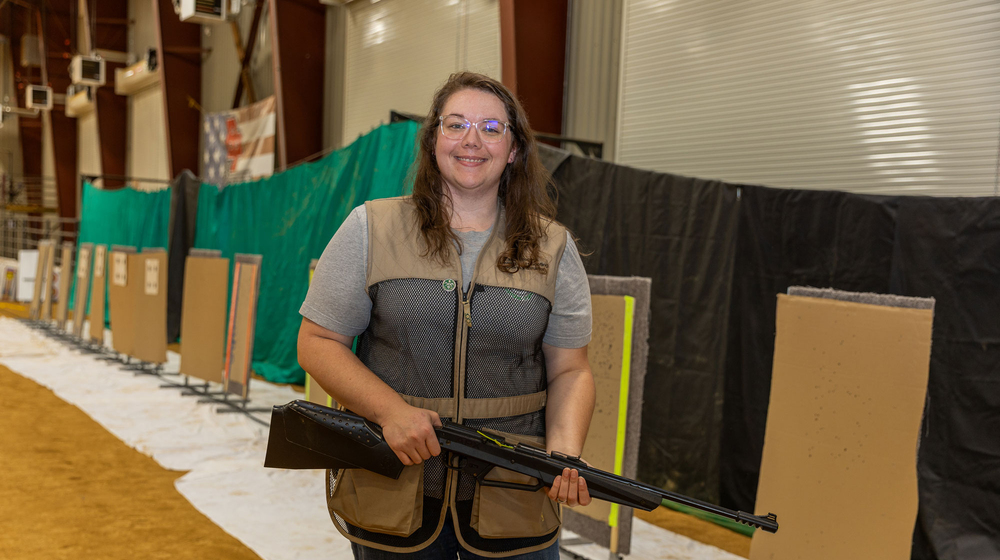 A person standing in an indoor shooting range and holding a firearm.