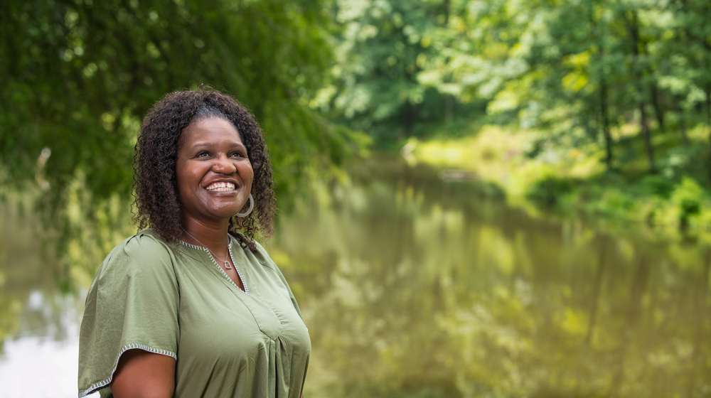 A person standing in front of a pond smiles at the sky.