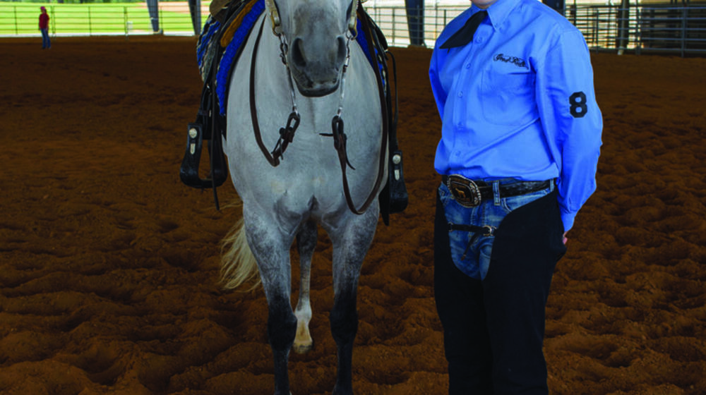 White horse stands beside teen boy with blue dress shirt and black cowboy hat