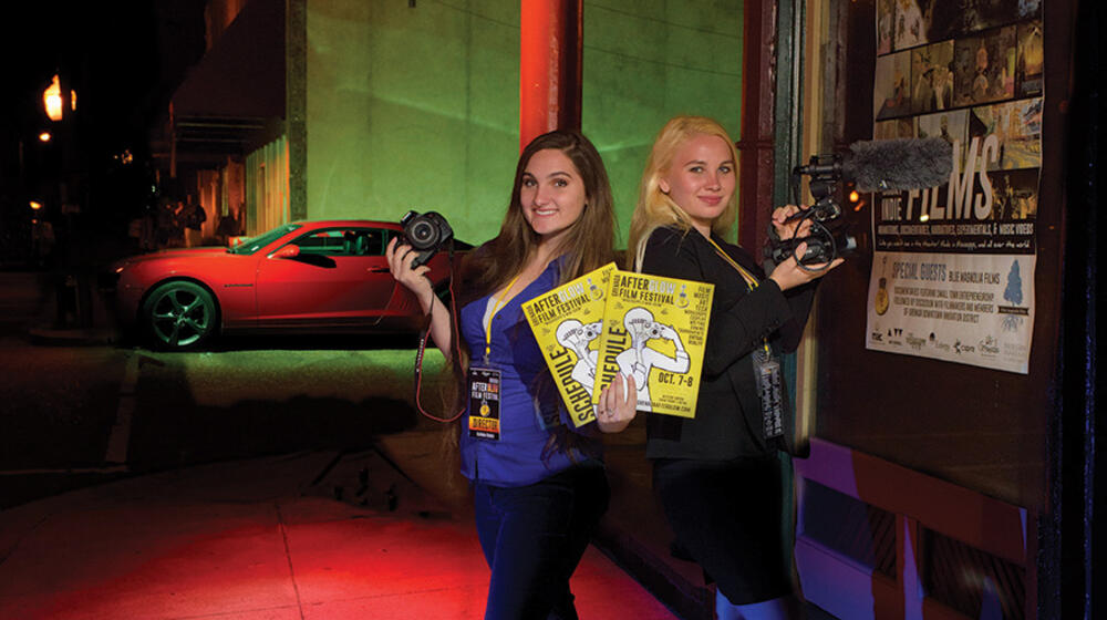 Two teenage girls holding cameras and yellow posters.