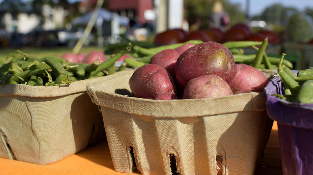 Red potatoes in a biodegradable basket are flanked on either side by green snap beans.